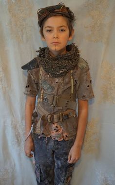 a young boy dressed up in an old fashion outfit with chains and leathers on his shoulders