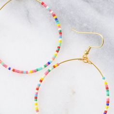 You asked for bigger beaded hoops and Libby & Smee answered! These dangly seed bead hoop earrings are the pieces you'll grab every day when you want a little something fun without a lot of fuss. Bonus: They look great dressed up or super casual. It's no surprise that they've become the Libby & Smee cult favorite. beaded hoops with tiny glass seed beads available in two large sizes: BIG, a teardrop shape approximately 1.75 inches wide and 2.75 inches long, or BIGGER, a circle shape 2.25 inches wi Star Charm Necklace, Plastic Earrings, Rainbow Beads, Rainbow Earrings, Earring Cards, Beading Wire, Metallic Pink, Beaded Hoop Earrings, Bohemian Earrings