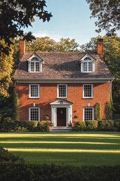 a red brick house with white trim and two story windows on the front, surrounded by lush green grass