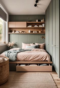 a bed sitting under a window next to a wooden shelf filled with dishes and cups