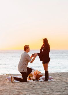 a man kneeling down next to a woman on top of a sandy beach