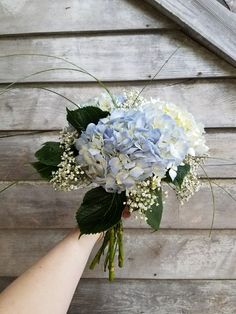 a bouquet of blue and white flowers is being held by a person's hand