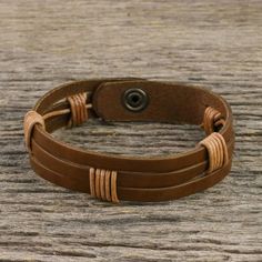 Chaloemphon of Thailand presents this men's leather wristband bracelet. The light brown leather has three horizontal slits. The artisan has wrapped two sections in black leather cord in artful intervals adding to the bracelet's texture and visual impact. The bracelet closes with a brass snap. Brown Leather Wrap Bracelet For Gift, Brown Leather Wrap Bracelet Gift, Brown Leather Wrap Bracelet As Gift, Adjustable Waxed Leather Bracelet, Adjustable Brown Leather Bracelet With Waxed Finish, Adjustable Rugged Leather Bracelet, Adjustable Distressed Brown Leather Bracelet, Rustic Adjustable Leather Bracelet With Waxed Finish, Adjustable Brown Leather Sweatband Wristband