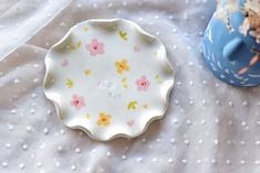 a white plate with pink flowers on it next to a blue vase and polka dot table cloth