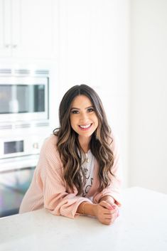 a woman sitting at a kitchen table in front of an oven and microwave with her arms crossed