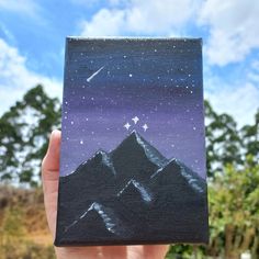 a hand holding up a small piece of art with mountains and stars in the sky