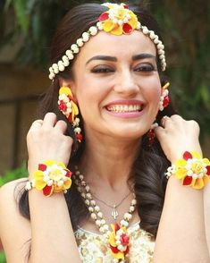 a woman with flowers in her hair and bracelets around her neck smiling at the camera