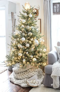 a christmas tree with white balls and lights in the corner of a cozy living room