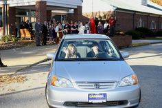 a silver car driving down a street with people in the back seat and onlookers