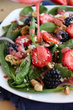 a salad with strawberries, blackberries, spinach and nuts on a white plate