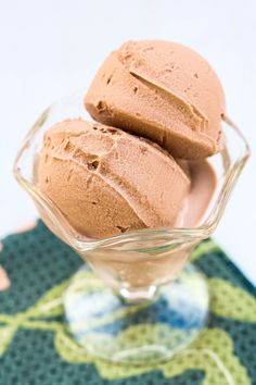 three scoops of chocolate ice cream in a glass bowl on a green place mat