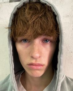 a young man with brown hair and blue eyes wearing a hoodie over his head