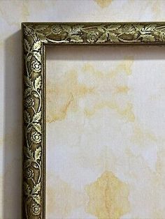 an ornate gold frame hanging on the wall with a white and beige marbled background