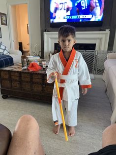 a little boy in a kimono holding a yellow stick while standing in front of a tv