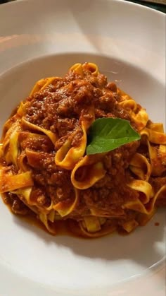 a white plate topped with pasta covered in sauce and meat next to a green leaf