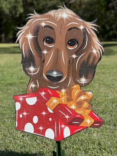 a cardboard dachshund holding a red present in it's mouth on top of a green lawn