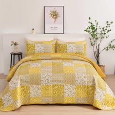 a bed with yellow and white bedspread in a room next to a potted plant