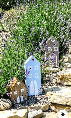 two small houses made out of cardboard sitting in the middle of some rocks and flowers