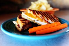 a grilled cheese sandwich with carrots and pickles sits on a blue plate