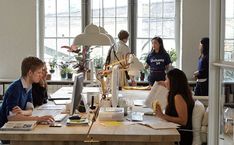 a group of people sitting around a table working on laptops and papers in an office