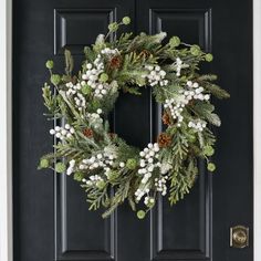 a christmas wreath on the front door with pine cones, berries and mists hanging from it