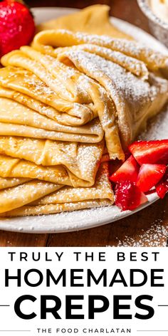 a white plate topped with crepes covered in powdered sugar and strawberries