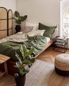 a bed with green sheets and pillows next to a plant in a pot on the floor