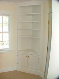 an empty room with white bookcases in the corner and windows on both sides