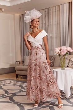 a woman standing in a room wearing a dress with flowers on it and a hat