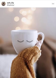 a person holding a coffee cup with eyelashes on it's face in front of a christmas tree