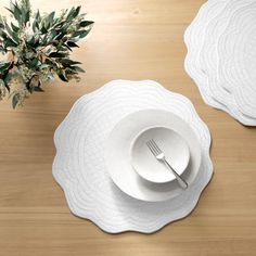 two white plates with silverware are on a wooden table next to a potted plant