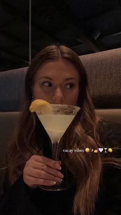 a woman holding a martini glass with a lemon wedge sticking out of it's mouth