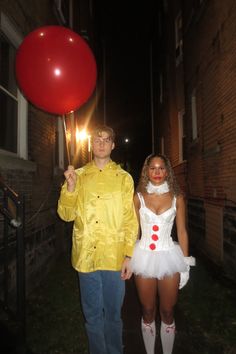 a man and woman dressed up as clowns holding a red balloon in the dark