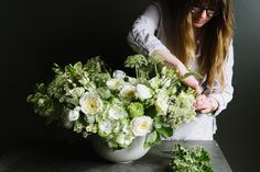 a woman arranging flowers in a white vase