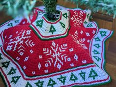 a crocheted christmas tree skirt on top of a table next to a potted plant