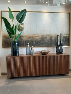 two vases and a plant sit on a wooden cabinet in front of a painting