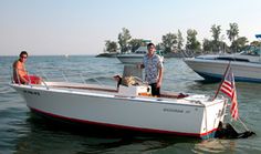 two men and a dog on a small boat in the water with other boats behind them