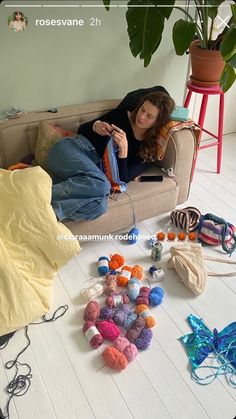 a woman sitting on a couch with lots of crochet and knitting supplies all around her