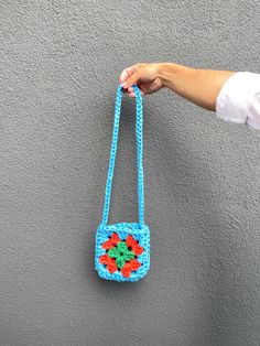 a hand holding a blue crocheted purse with flowers on it's handle