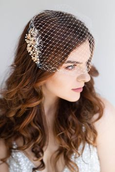 a woman wearing a birdcage veil with flowers on it's head and hair comb