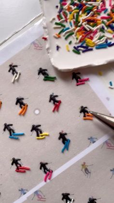 there are many small toy figures on the table next to a pen and paper with colored sprinkles