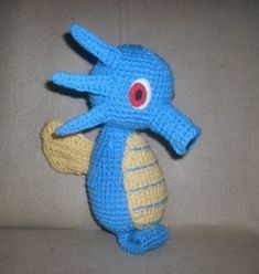 a crocheted blue and yellow stuffed animal with red eyes sitting on a white surface