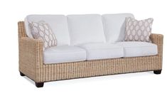 a wicker couch with white cushions and pillows on it's armrests