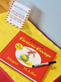 a red and yellow book sitting on top of a table next to a white envelope