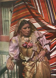 an old photo of a woman dressed in traditional mexican garb sitting on a porch