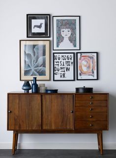 a wooden dresser sitting next to a wall with pictures on it