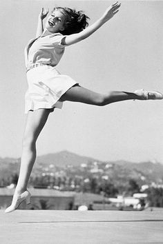 a woman is jumping in the air with her legs spread out and one leg up