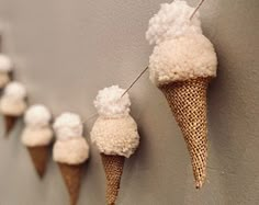 several cones with white fluffy balls hanging from them on a line against a gray wall