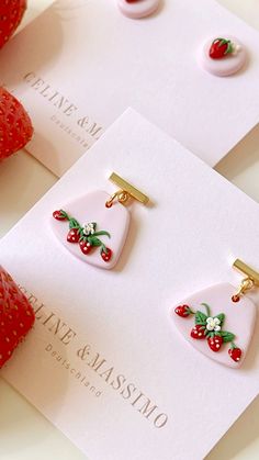 two strawberry shaped earrings sitting on top of a white card with strawberries in the background