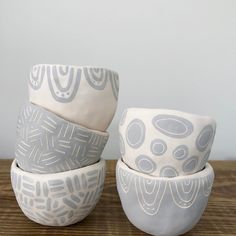 three white and gray bowls sitting on top of a wooden table